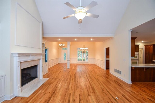 unfurnished living room featuring ornate columns, light hardwood / wood-style flooring, vaulted ceiling, a fireplace, and ceiling fan with notable chandelier