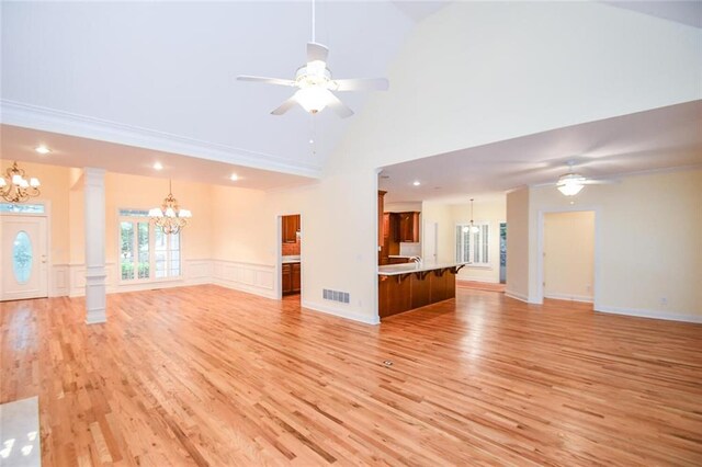 unfurnished living room featuring lofted ceiling, ceiling fan with notable chandelier, crown molding, light wood-type flooring, and decorative columns