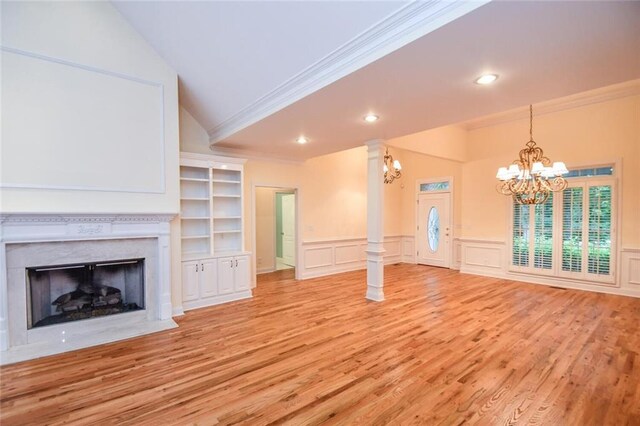 unfurnished living room featuring built in shelves, ornamental molding, a fireplace, a notable chandelier, and decorative columns