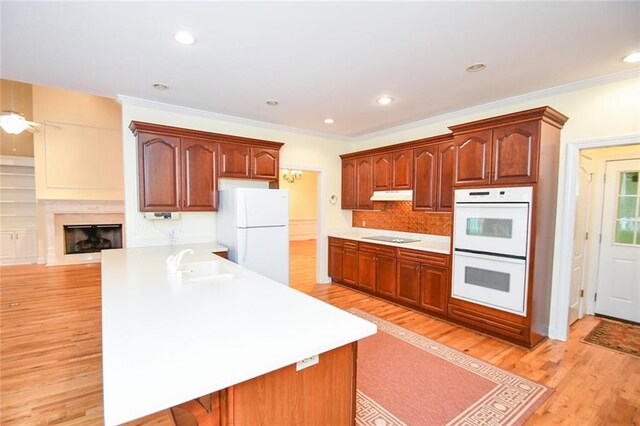 kitchen with white appliances, sink, light hardwood / wood-style flooring, ornamental molding, and kitchen peninsula