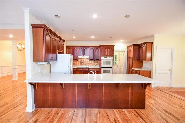 kitchen featuring kitchen peninsula, white appliances, a breakfast bar area, and backsplash