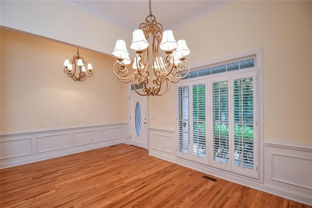 unfurnished dining area with wood-type flooring, an inviting chandelier, and crown molding