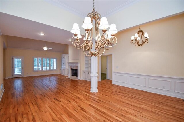 unfurnished living room with ceiling fan with notable chandelier, light hardwood / wood-style flooring, ornamental molding, and a premium fireplace