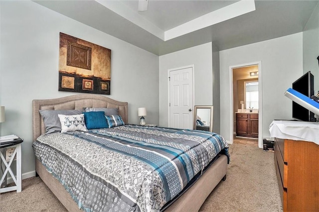 bedroom with a tray ceiling, light colored carpet, baseboards, and ensuite bathroom