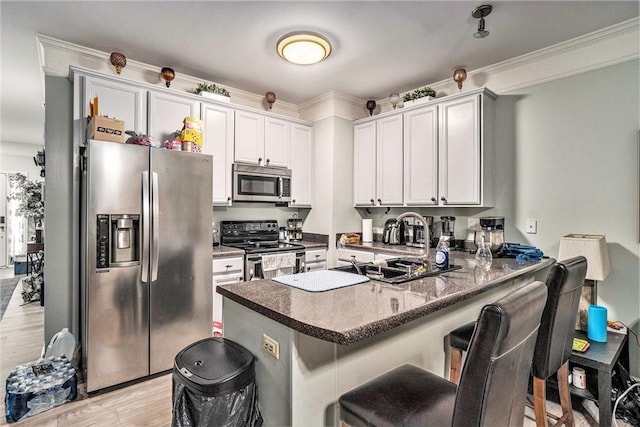 kitchen with a peninsula, a breakfast bar, white cabinetry, light wood-style floors, and appliances with stainless steel finishes