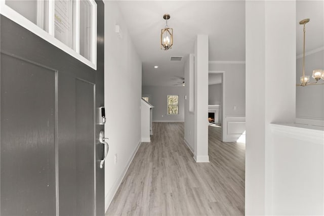 entrance foyer with a warm lit fireplace, visible vents, baseboards, light wood-type flooring, and ceiling fan with notable chandelier