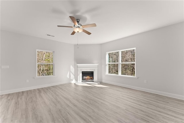 unfurnished living room featuring light wood-type flooring, baseboards, visible vents, a high end fireplace, and a ceiling fan