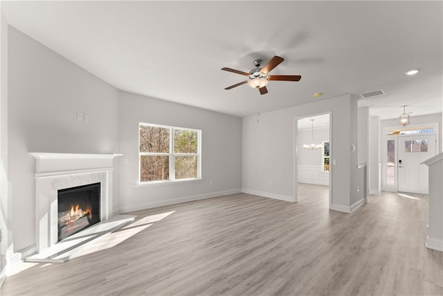 unfurnished living room with ceiling fan with notable chandelier, light wood-style floors, a fireplace, and baseboards