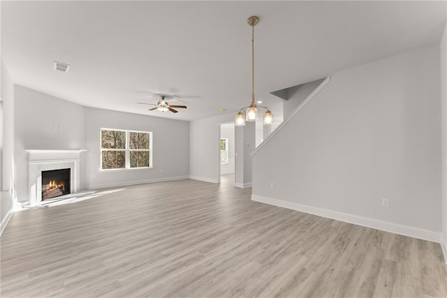 unfurnished living room with visible vents, a high end fireplace, baseboards, ceiling fan, and light wood-style floors