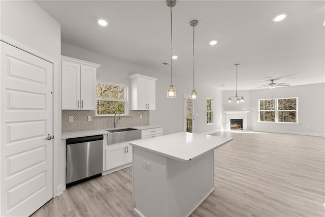 kitchen with light countertops, a sink, a kitchen island, dishwasher, and a ceiling fan