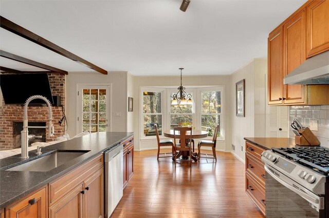 kitchen featuring light wood-style flooring, a fireplace, a sink, appliances with stainless steel finishes, and backsplash