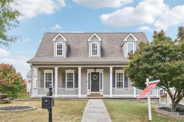 new england style home with a front lawn, a porch, and roof with shingles