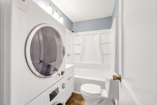 bathroom with tub / shower combination, toilet, stacked washing maching and dryer, wood finished floors, and vanity