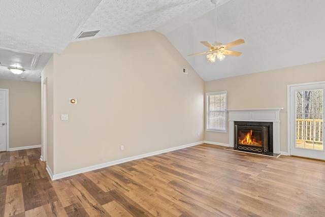 unfurnished living room featuring vaulted ceiling, a healthy amount of sunlight, a textured ceiling, and light hardwood / wood-style floors