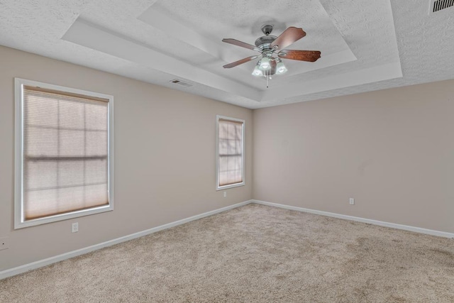 empty room with a raised ceiling, ceiling fan, light carpet, and a textured ceiling