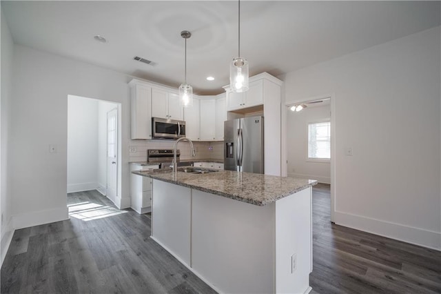 kitchen with white cabinetry, appliances with stainless steel finishes, a kitchen island with sink, and dark stone counters