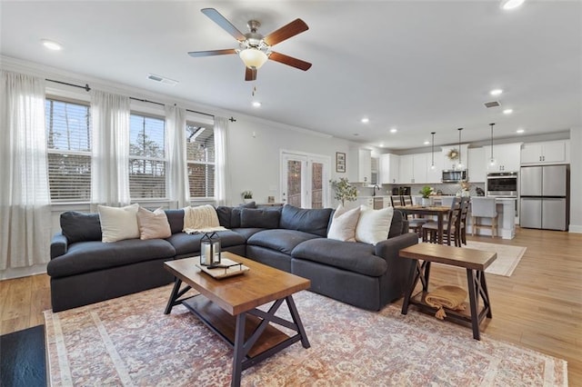 living room featuring crown molding, a ceiling fan, visible vents, and light wood finished floors