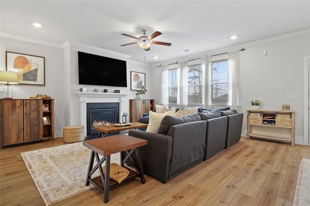 living area with visible vents, crown molding, ceiling fan, light wood-type flooring, and a glass covered fireplace