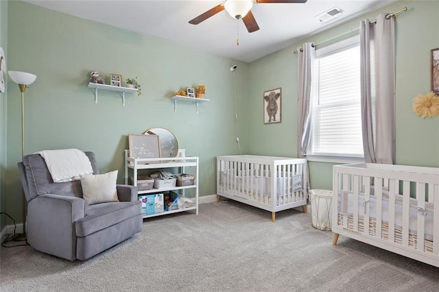 carpeted bedroom with baseboards, visible vents, a crib, and a ceiling fan