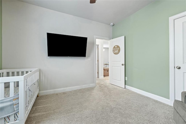 unfurnished bedroom with a nursery area, ceiling fan, baseboards, and carpet floors