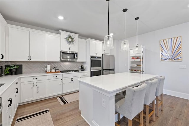 kitchen featuring light wood-style flooring, tasteful backsplash, a kitchen island, white cabinetry, and appliances with stainless steel finishes