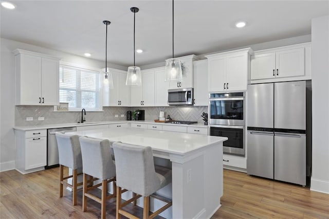 kitchen featuring a kitchen island, light countertops, light wood-style flooring, appliances with stainless steel finishes, and white cabinetry