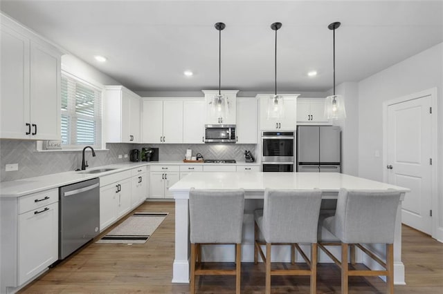 kitchen featuring a breakfast bar, a sink, a kitchen island, light wood-style floors, and appliances with stainless steel finishes