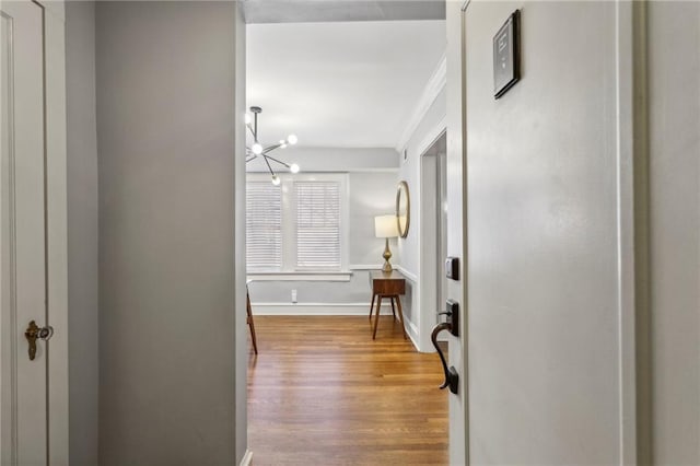 hallway featuring an inviting chandelier, light wood-style flooring, and baseboards