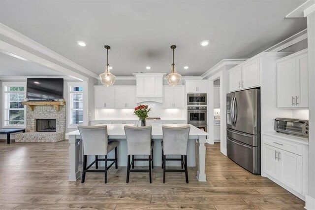 kitchen with appliances with stainless steel finishes, white cabinetry, tasteful backsplash, an island with sink, and a kitchen bar