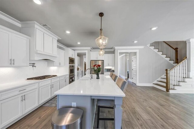 kitchen featuring white cabinetry, decorative light fixtures, a center island with sink, and appliances with stainless steel finishes