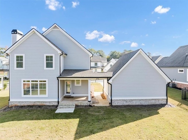 rear view of property with fence, a chimney, a lawn, a shingled roof, and a patio area