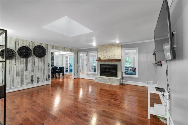 unfurnished living room featuring ornamental molding, hardwood / wood-style floors, baseboards, and a stone fireplace