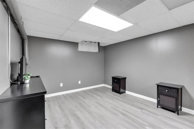 finished below grade area with a drop ceiling, light wood-type flooring, and baseboards