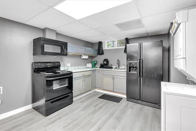 kitchen with black appliances, a sink, a paneled ceiling, light wood finished floors, and light countertops