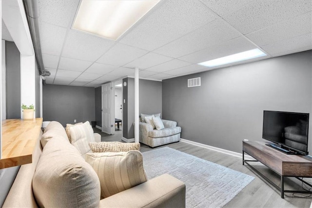 living area featuring wood finished floors, a drop ceiling, and baseboards