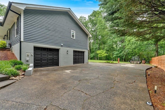 view of side of home featuring driveway, an attached garage, and stucco siding