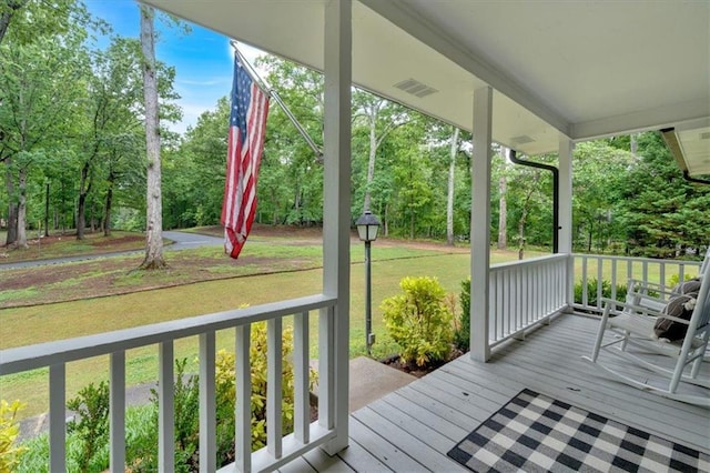 wooden deck with a porch, view of wooded area, and a lawn