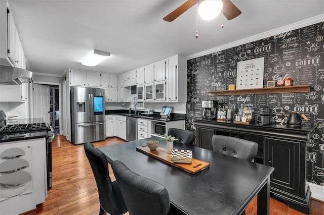 kitchen with appliances with stainless steel finishes, a sink, crown molding, dark countertops, and white cabinetry