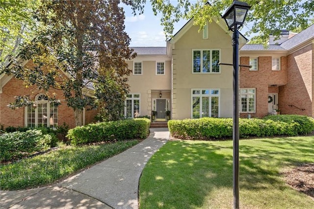 view of front of home featuring a front yard, brick siding, and stucco siding