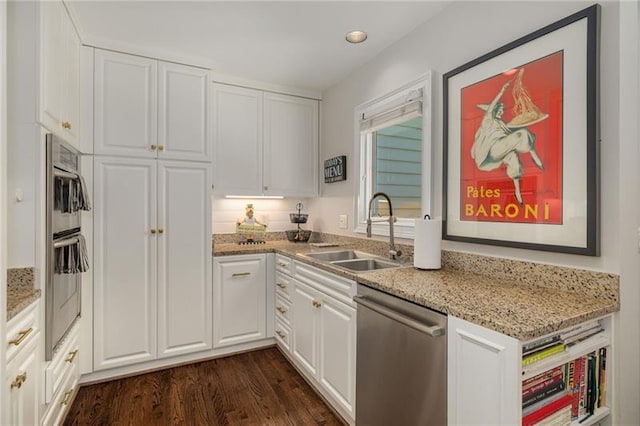 kitchen with a sink, appliances with stainless steel finishes, dark wood-style floors, and white cabinetry