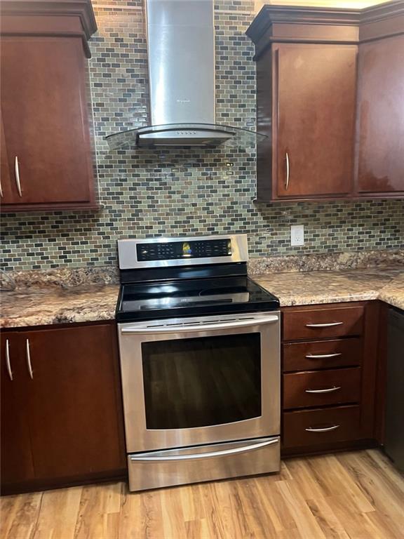 kitchen with stainless steel electric stove, dark brown cabinetry, light wood-style floors, wall chimney range hood, and backsplash