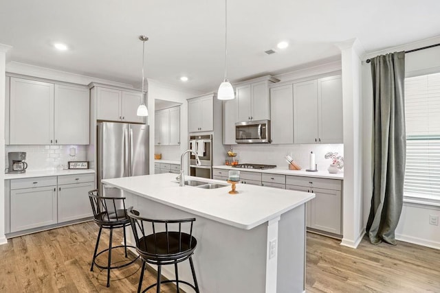 kitchen with light wood-type flooring, appliances with stainless steel finishes, pendant lighting, a kitchen island with sink, and decorative backsplash