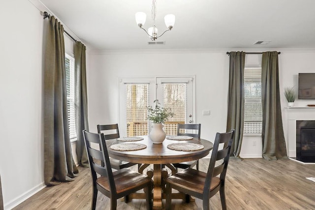 dining room featuring an inviting chandelier, ornamental molding, a wealth of natural light, and light wood-type flooring