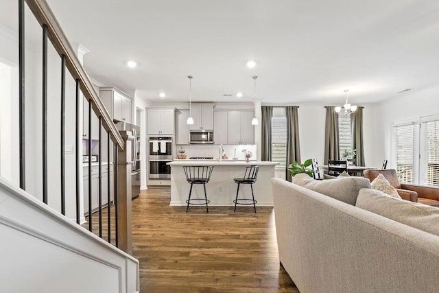 living room with crown molding, an inviting chandelier, sink, and dark wood-type flooring