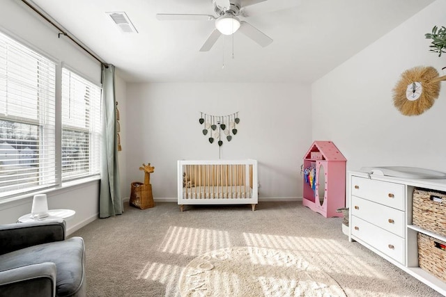 carpeted bedroom with multiple windows, a nursery area, and ceiling fan