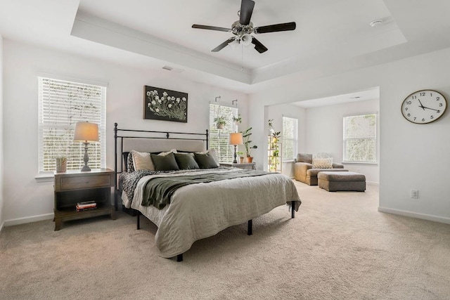 bedroom with ceiling fan, a tray ceiling, light colored carpet, and multiple windows