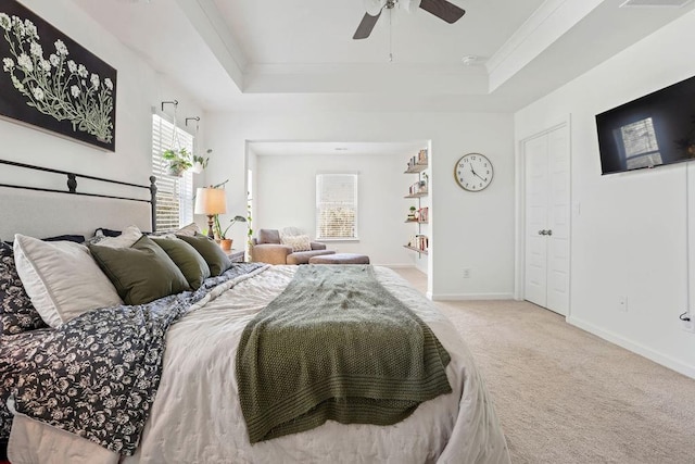 carpeted bedroom featuring multiple windows, a tray ceiling, ornamental molding, and ceiling fan