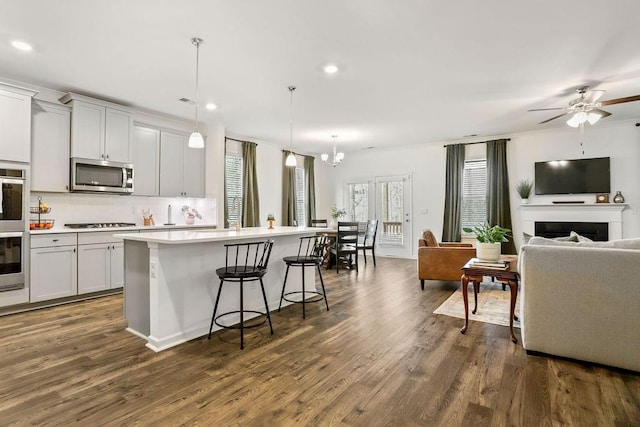 kitchen featuring a breakfast bar area, decorative light fixtures, appliances with stainless steel finishes, an island with sink, and white cabinets