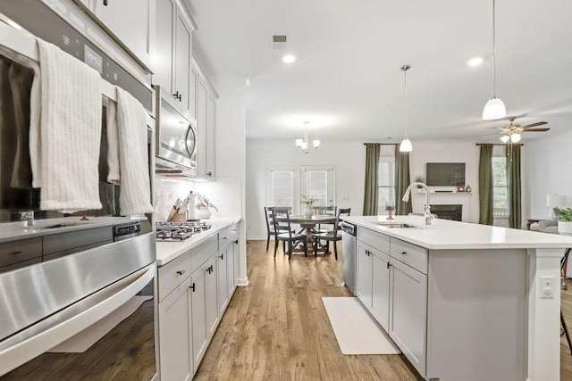 kitchen featuring sink, white cabinetry, hanging light fixtures, a center island with sink, and appliances with stainless steel finishes