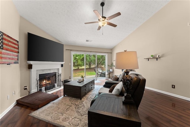 living area with wood finished floors, a warm lit fireplace, ceiling fan, and vaulted ceiling